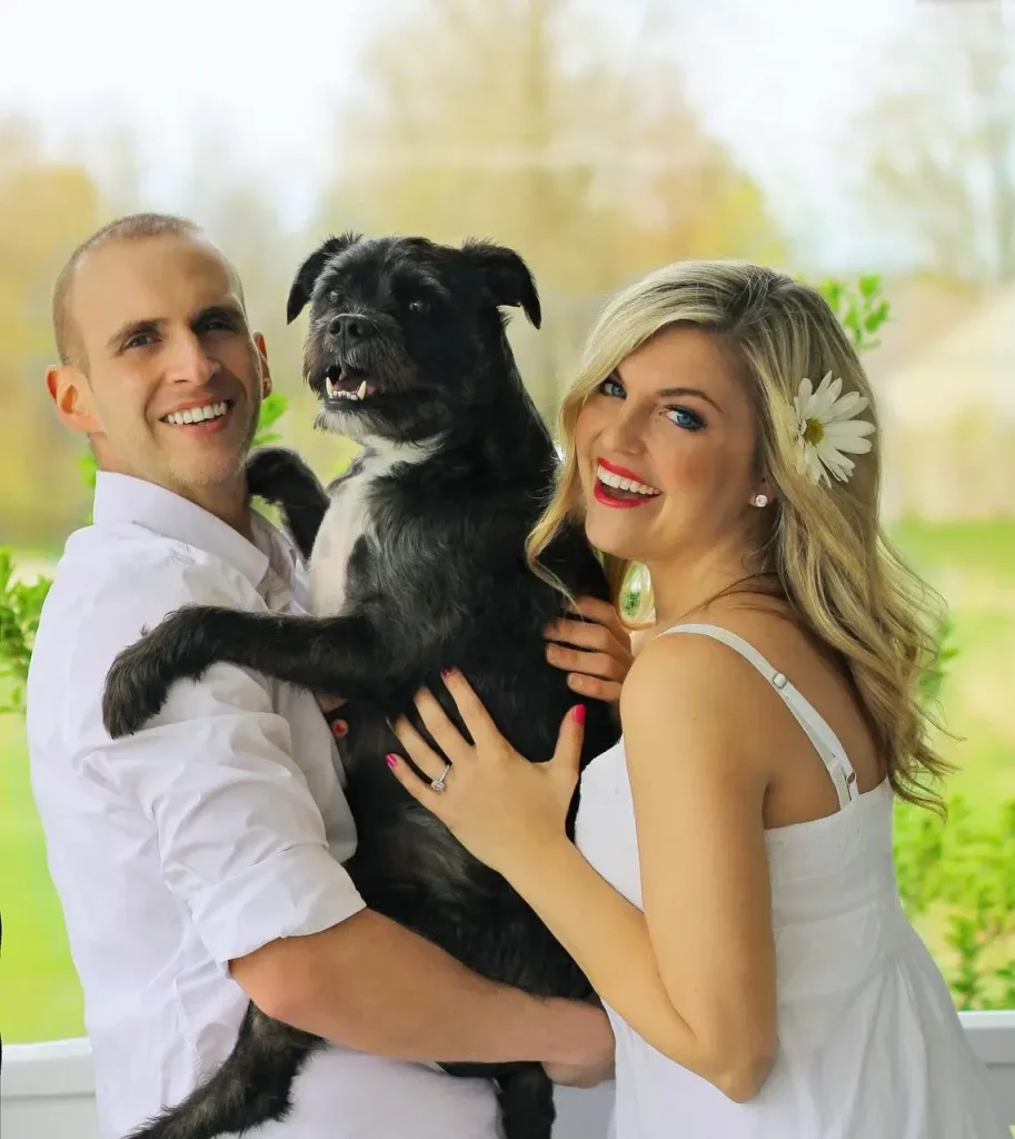 couple smiling pose with black dog - Canine United